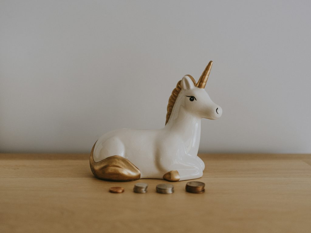 4 stacks of coins in front of a unicorn figurine.